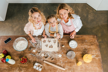 Wall Mural - top view of smiling child with mother and grandmother preparing christmas cookies at home and looking at camera