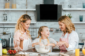 Wall Mural - happy little child preparing dough with mother and grandmother at home