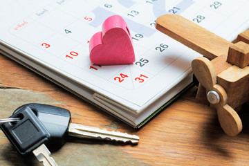 Love traveling holiday concept. Red heart on calendar and key car and wooden plane on wooden table. summer day.