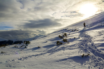 Wide view on the snowy hill with footprints and far away hiker walking up with backpack in the mountains