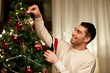 © Syda Productions - winter holidays and people concept - happy man decorating christmas tree at home