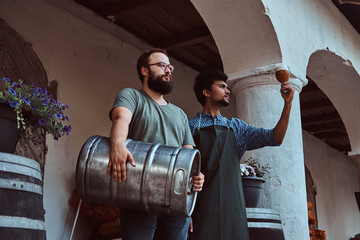 Wall Mural - Two brewers in apron standing outdoors checking the quality of brewed drink at brewery factory.