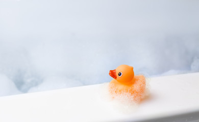 Orange playful rubber duck in a bubble bath, light blue background with bubbles. Kids spa concept. Children`s bath time concept.