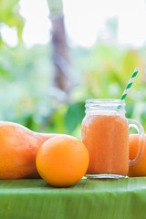 Wall Mural - Tropical exotic pineapple and papaya fruits with jar smoothie shake juice drink outdoors with palm leaves