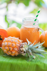 Wall Mural - Tropical exotic pineapple and papaya fruits with jar smoothie shake juice drink outdoors with palm leaves