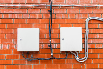 A two white box with an electric high-voltage cable on a red brick wall.