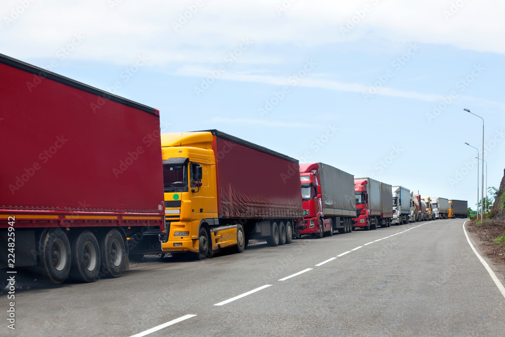 Queue of trucks passing the international border, red and different colors trucks in traffic jam on the road - obrazy, fototapety, plakaty 