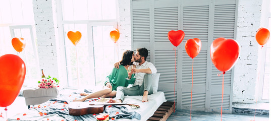 Love in every moment. Cute young beautiful couple are hugging, kissing and relax while they celebrating the St. Valentines day at home