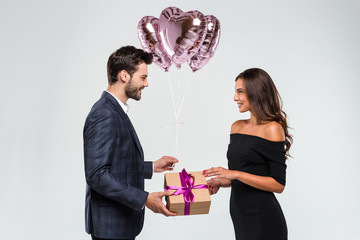 Wall Mural - Happy birthday my love! Young handsome men giving a gift box to his girlfriend while standing against white background