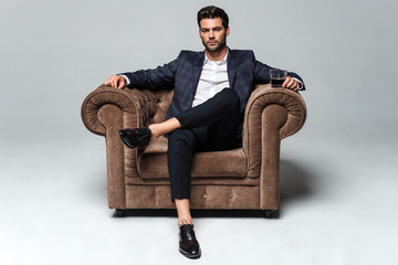 little stylish rest. full length of handsome young man looking at camera while sitting against white
