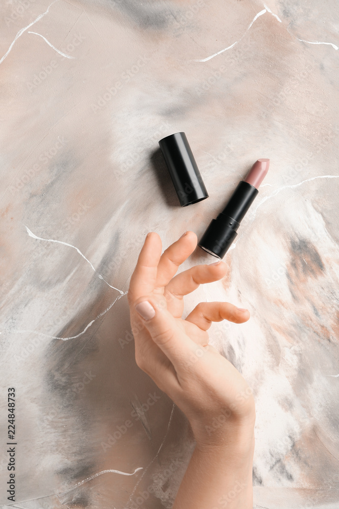 Female hand and light lipstick on table