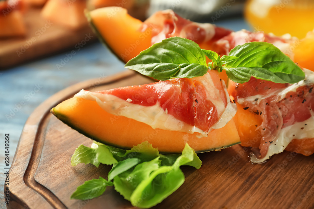 Delicious melon with prosciutto and basil on wooden board, closeup