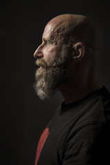 a bearded man with a bald head side view and dark background