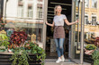 © LIGHTFIELD STUDIOS - attractive florist in apron opening door of flower shop