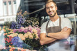 © LIGHTFIELD STUDIOS - view through window of handsome florist standing with crossed arms in flower shop and looking at camera