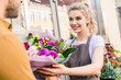 © LIGHTFIELD STUDIOS - smiling attractive florist giving bouquet to customer near flower shop