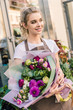 © LIGHTFIELD STUDIOS - attractive florist holding beautiful bouquet of chrysanthemums near flower shop and looking away