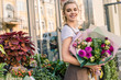 © LIGHTFIELD STUDIOS - smiling florist holding beautiful bouquet of chrysanthemums near flower shop and looking at camera