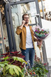 © LIGHTFIELD STUDIOS - smiling handsome man going out from flower shop with bouquet and talking by smartphone