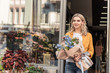 © LIGHTFIELD STUDIOS - beautiful woman going out from flower shop with wrapped bouquet and looking away