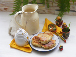 Wall Mural - Traditional russian cuisine : pancakes on plate with oak flakes on  shabby white wooden background with rustic milk jug, honey, yellow napkins and nesting dolls matrioshka