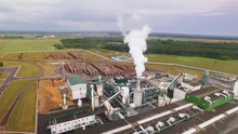 Smoke Or Steam Scatters, Comes Out Of Chimney, Tube, Pipe. Storage, Warehouse Of Woodworking Plant. Factory Pollutes The City, Burns Logs, Timber Or Trees. Aerial View. Air Shoot