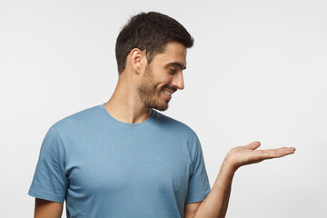 Wall Mural - young smiling man isolated on gray background wearing casual blue t-shirt and demonstrating somethin