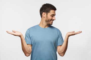 Wall Mural - young handsome male choosing between two different options, holding 2 hands, isolated on gray backgr