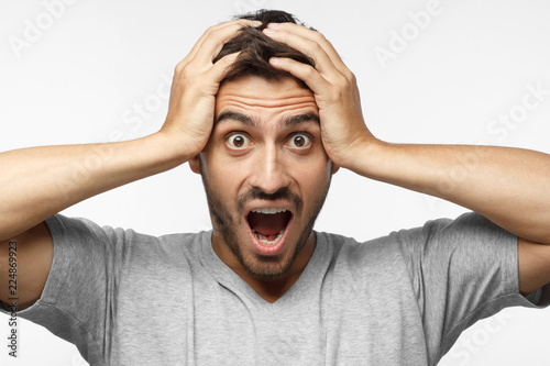 Fotografia, Obraz Close up shot of shocked young man with round eyes, open mouth and hands pressed