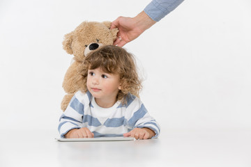 Portrait of happy joyful beautiful little boy sitting with laptop and teddy bear toy , studio shot on white