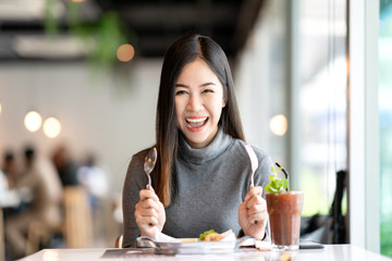 young attractive asian woman holding fork and spoon feeling hungry, excited, happy and ready to eat 