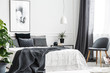 Modern, gray chair with wooden legs by a window of a bright bedroom interior with a dark gray blanket on a comfy bed