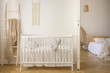 © Photographee.eu - Wooden crib with cushions standing in real photo of white kid room interior with blanket on ladder and macrame on the wall
