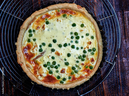 Fotografía Smoked trout, goat cheese and peas quiche, set on a cooling rack, on a dark bro