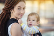 © Artem - Modern happy mother with baby son in ergo backpack walking in Sunny summer day. Concept of the joy of motherhood