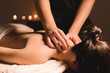 canvas print picture - Men's hands make a therapeutic neck massage for a girl lying on a massage couch in a massage spa with dark lighting. Close-up. Dark Key