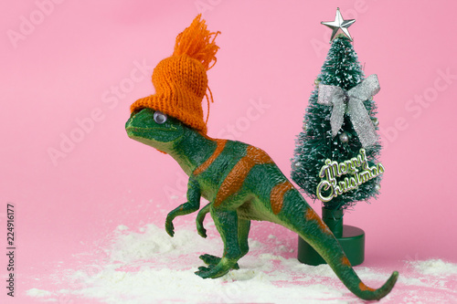 Photo funny green dinosaur toy in littleorange knitted hat near little christmas tre
