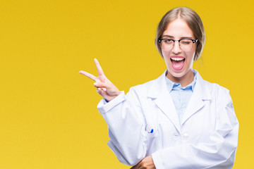 Poster - Beautiful young blonde doctor woman wearing white coat over isolated background smiling with happy face winking at the camera doing victory sign. Number two.