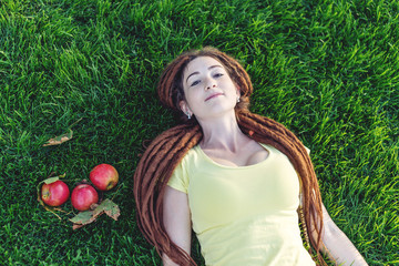 Modern young girl with a hairstyle dreadlocks in the Park on a green meadow eating apples and enjoying the autumn mood