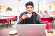 © dianagrytsku - Young indian guy drinking coffee while computing at a student cafe