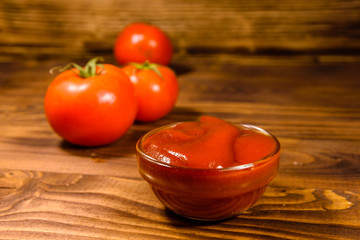 Ripe tomatoes and ketchup on wooden table