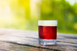 Glass Of Berry Juice On An Old Wooden Table On Garden Background On Bright Sunny Day Or At Dawn. Cranberry, Cherry, Raspberry Or Grape Cold Juice In Misted And Covered With Drops Of Water Glass Cup.
