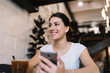 © Oleksii - Young attractive woman with beautiful face and smile holding mobile phone, downloading application in loft cafe. Social media marketing. Female blogger write blog post using smartphone and internet.