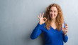 © Krakenimages.com - Young redhead woman over grey grunge wall drinking water doing ok sign with fingers, excellent symbol