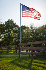 The American flag is developed on the flagpole in the courtyard of the house at sunset.