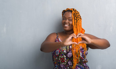 Sticker - Young african american woman over grey grunge wall wearing orange braids smiling in love showing heart symbol and shape with hands. Romantic concept.