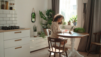 charming young woman typing on laptop computer in a kitchen.