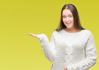 Young beautiful caucasian woman wearing winter sweater over isolated background smiling cheerful presenting and pointing with palm of hand looking at the camera.