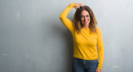 Sticker - Middle age hispanic woman over grey wall wearing glasses confuse and wonder about question. Uncertain with doubt, thinking with hand on head. Pensive concept.