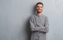 Young Adult Man Standing Over Grey Grunge Wall Happy Face Smiling With Crossed Arms Looking At The Camera. Positive Person.